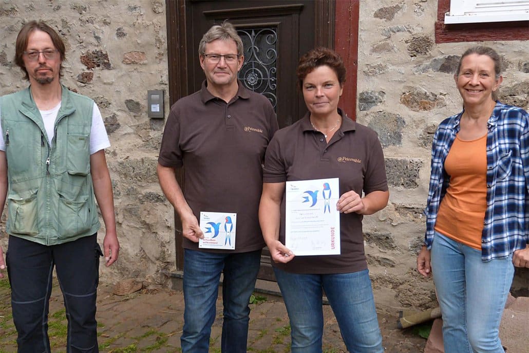 Roland Graf und Ulrike Balzer (re.) vom Nabu Lich überreichen Sonja und Andreas Feucht Urkunde und Plakette "Schwalbenfreundliches Haus"